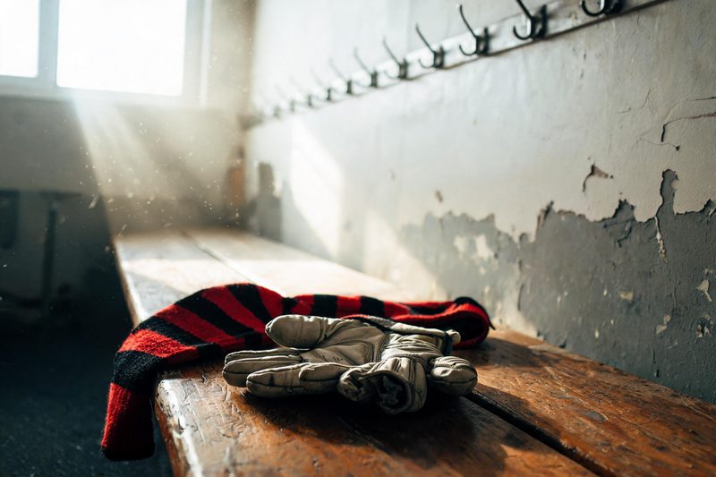 Roter und schwarzer Fanschal und Torwarthandschuhe auf einer Holzbank in einer Garderobe
